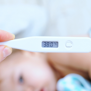 Frau liest den Wert auf dem Fieberthermometer ab, um herauszufinden, ob es sich um erhöhte Temperatur oder Fieber handelt.